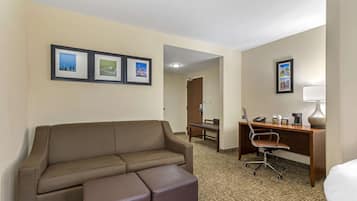 Ein Hotelzimmer mit einer Couch, einem Schreibtisch mit Stuhl, einem Bett und gerahmten Bildern an der Wand.