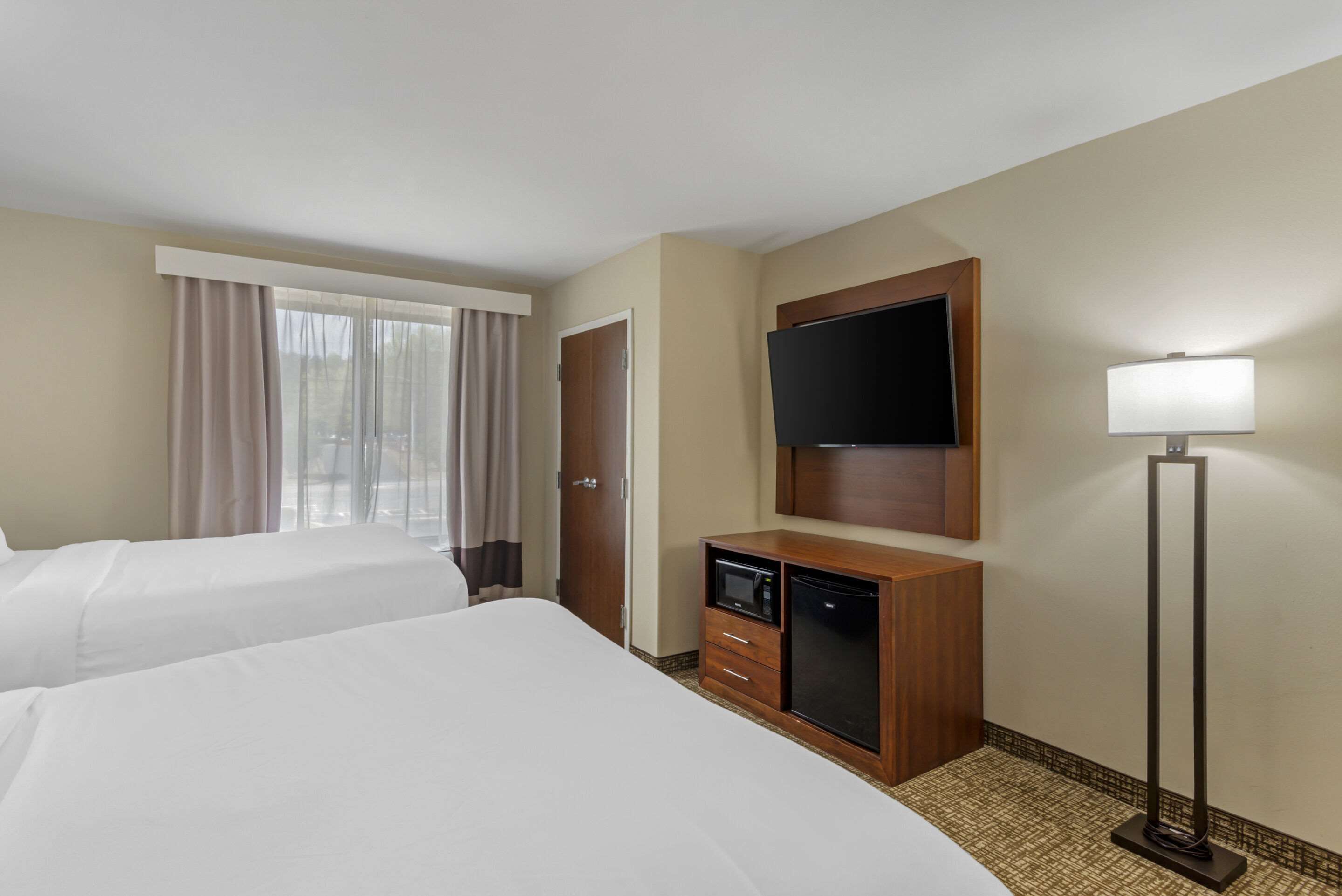 A hotel room with two beds, a TV, a minibar, and a lamp.