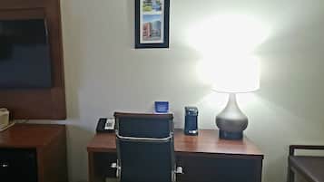 Une chambre d’hôtel équipée d’un bureau, d’une chaise, d’une lampe, d’une poubelle et d’un tableau encadré au mur.