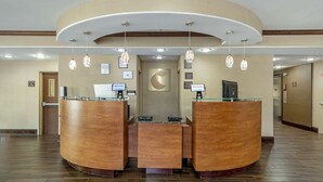 A reception area with a curved wooden desk, two computer monitors, and a glass-top desk. - Comfort Suites At Kennesaw State University (Kennesaw)