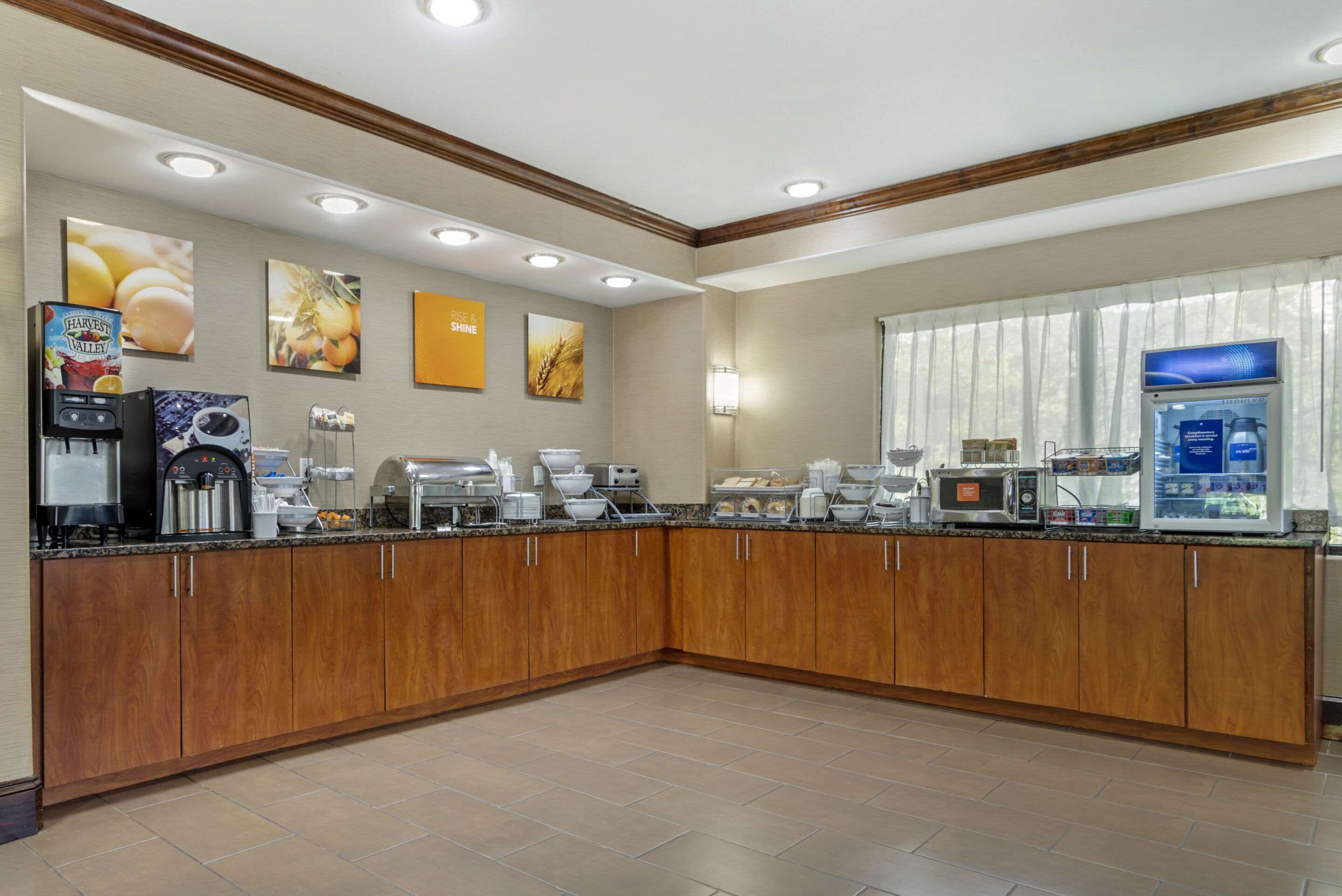 A hotel kitchen with a breakfast bar, coffee machines, and a refrigerator.