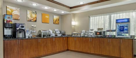 A hotel kitchen with a breakfast bar, coffee machines, and a refrigerator.