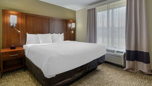 A hotel room with a large bed, a nightstand with a clock, a wall-mounted lamp, and a window with curtains. - Comfort Suites At Kennesaw State University (Kennesaw)