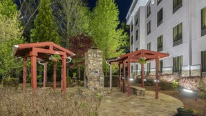 A stone-paved courtyard with red pergolas, a stone wall, and a building with multiple windows in the background. - Comfort Suites At Kennesaw State University (Kennesaw)