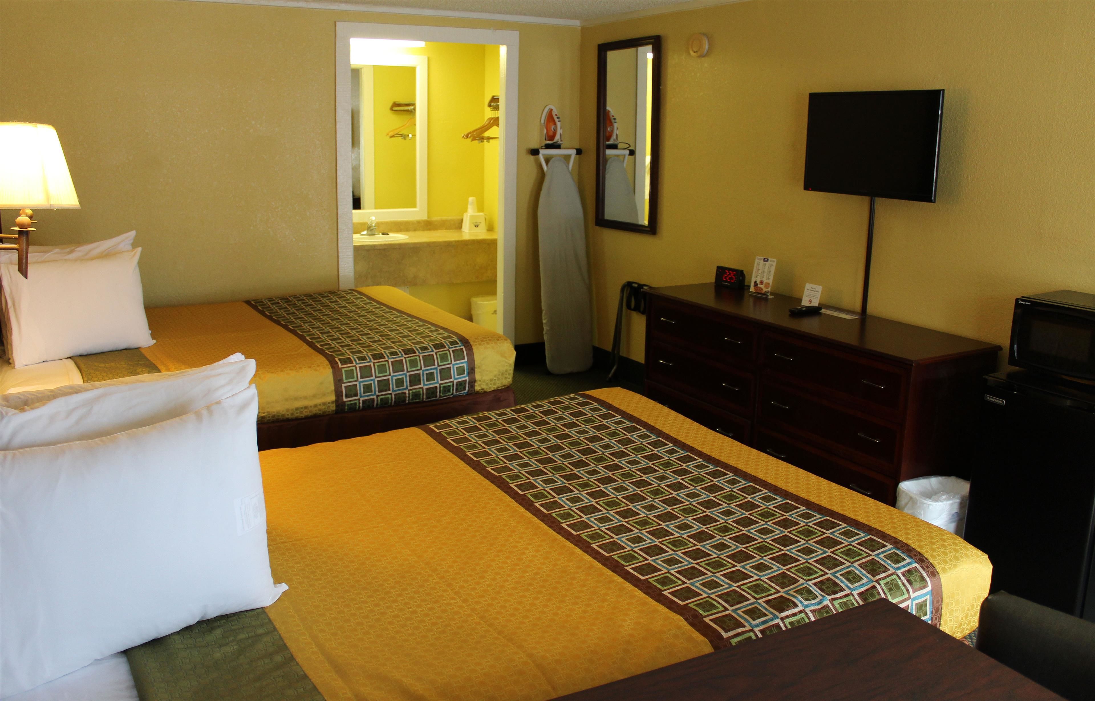 Habitación de hotel con dos camas, televisión, cómoda y baño visible a través de una puerta abierta.
