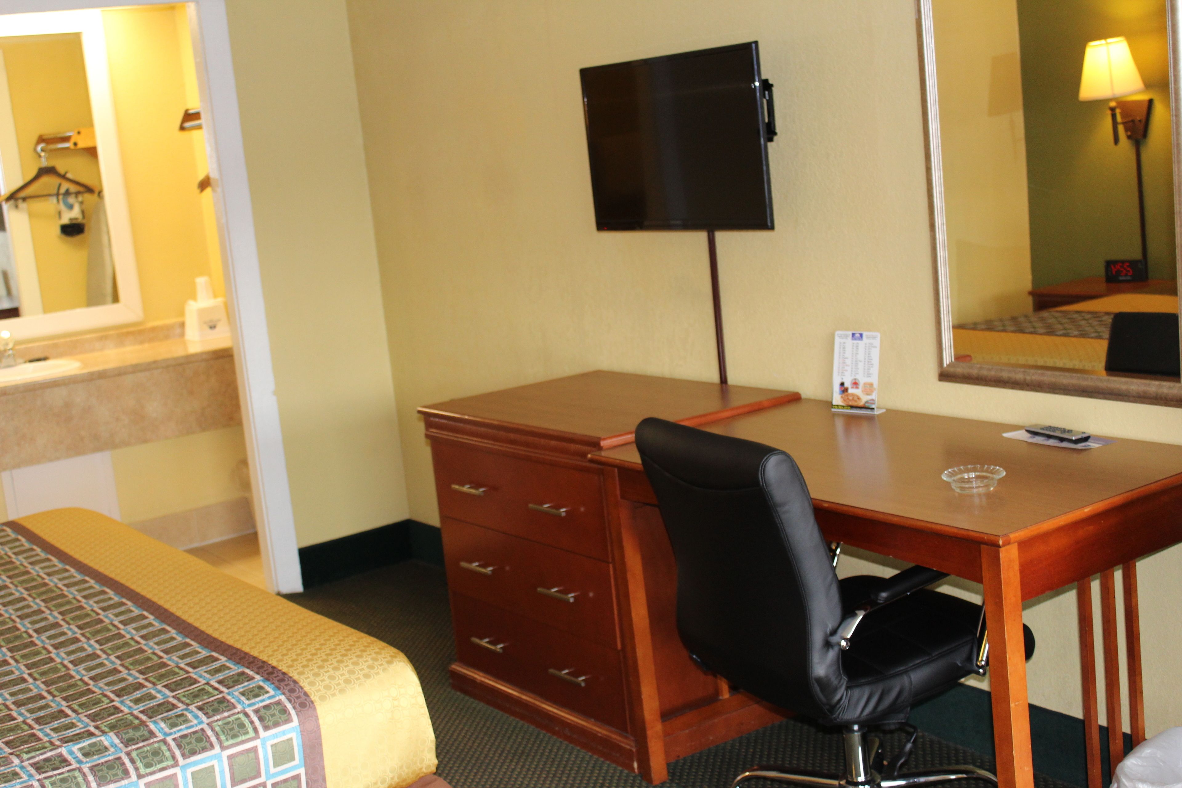 Ein Hotelzimmer mit Bett, Schreibtisch, Stuhl, Fernseher, Spiegel und Kommode.