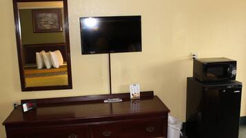 Habitación de hotel con cómoda de madera, televisor de pantalla plana en la pared, microondas sobre una mesita y un cubo de basura.