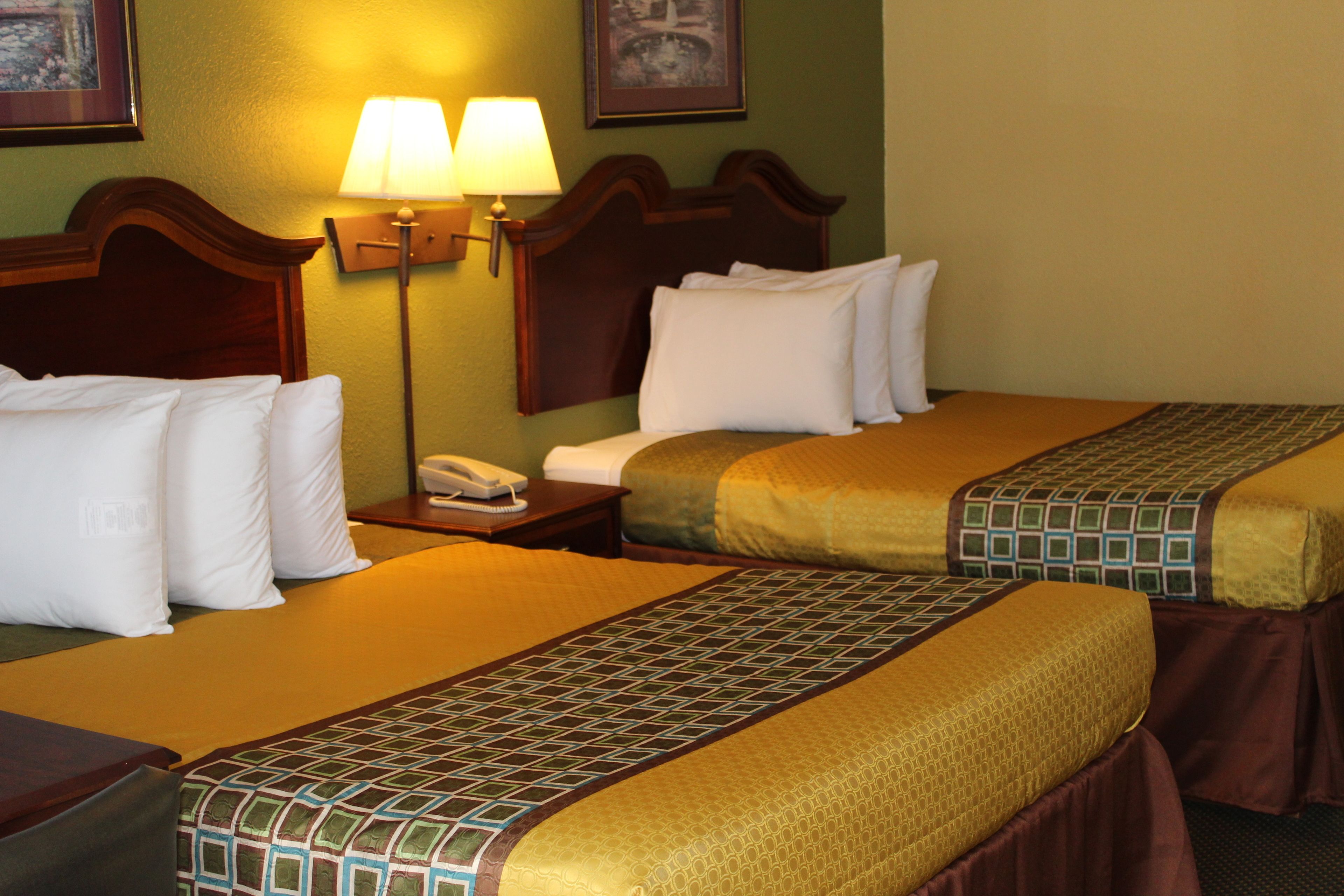 A hotel room with two beds, each with a patterned bedspread, a nightstand with a lamp, and a framed picture on the wall.