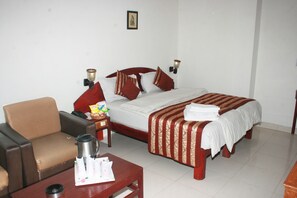 A hotel room with a bed, a chair, a table, and a nightstand. - South Indian Hotel (New Delhi)