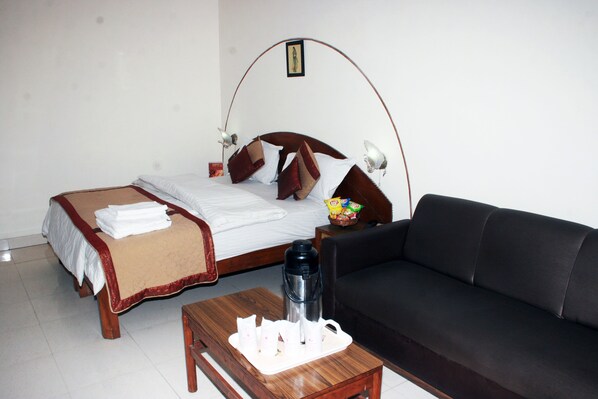 A hotel room with a bed, a black sofa, a coffee table with a tray of items, and a wall-mounted lamp.