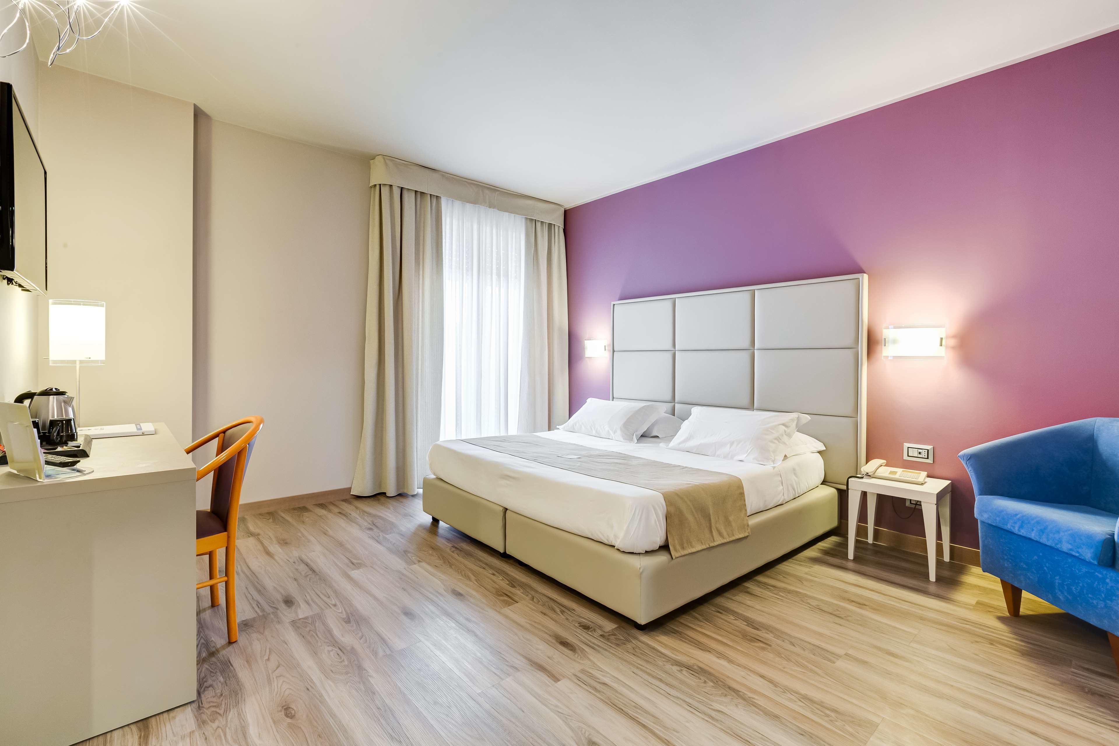 Una camera d'albergo con un letto, una scrivania, una sedia, un tavolino e una poltrona blu.