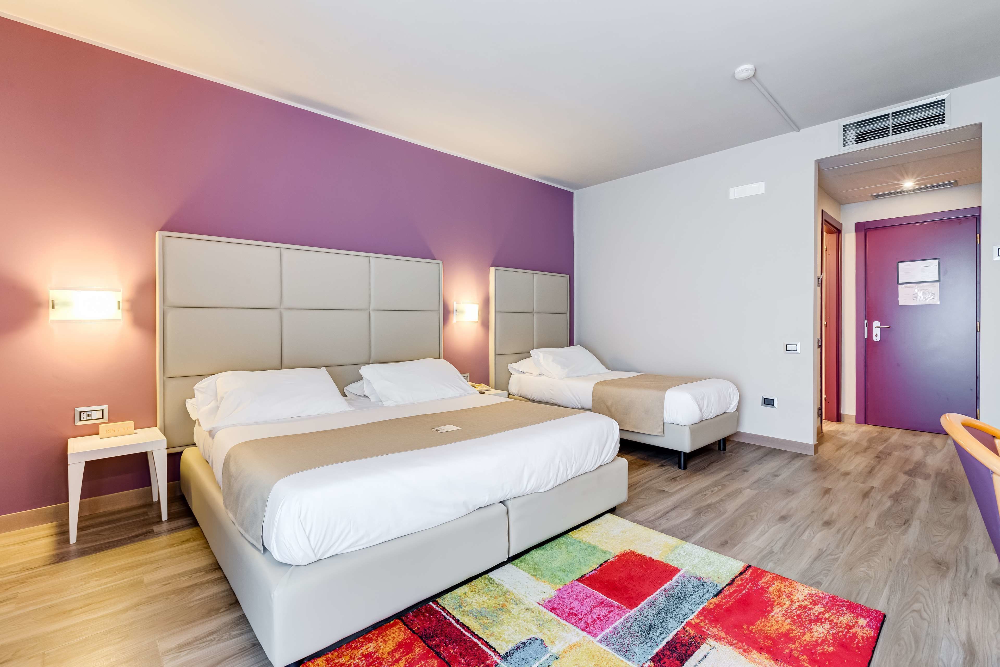 A hotel room with two beds, a colorful rug, and a purple wall.