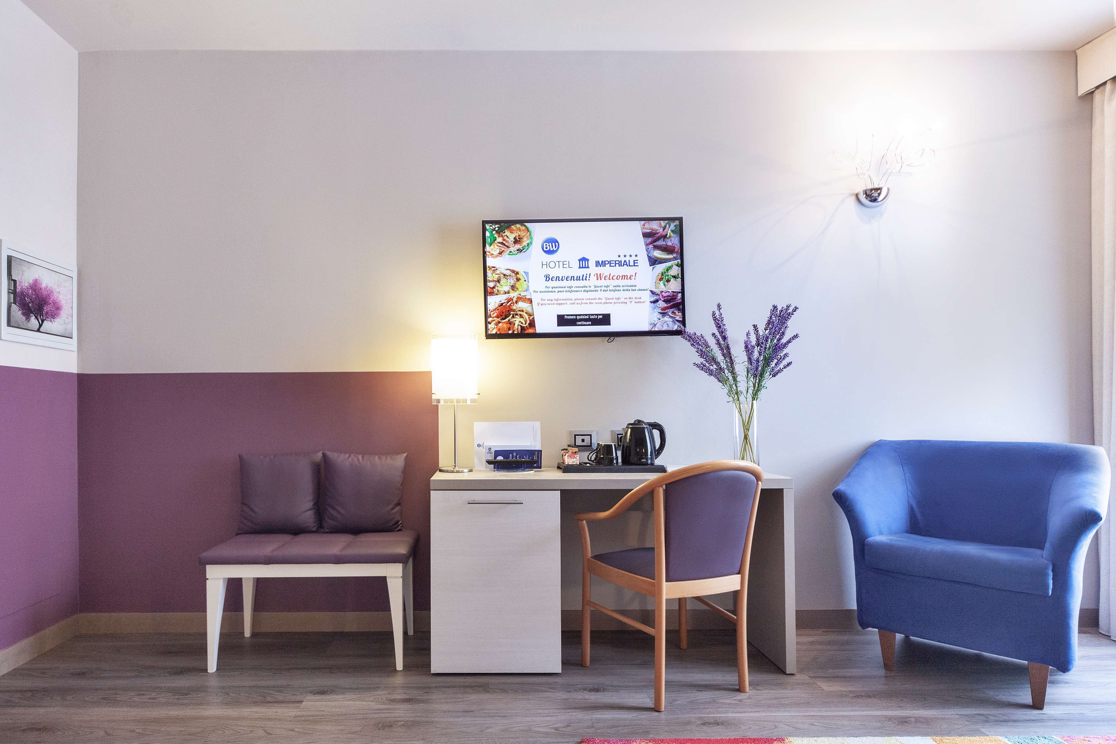 Ein Hotelzimmer mit Schreibtisch, Stuhl, Sofa und Fernseher, der eine Willkommensnachricht zeigt.