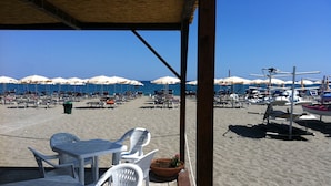 Un café situé en bord de mer, avec une terrasse, des parasols et une vue sur l’océan.