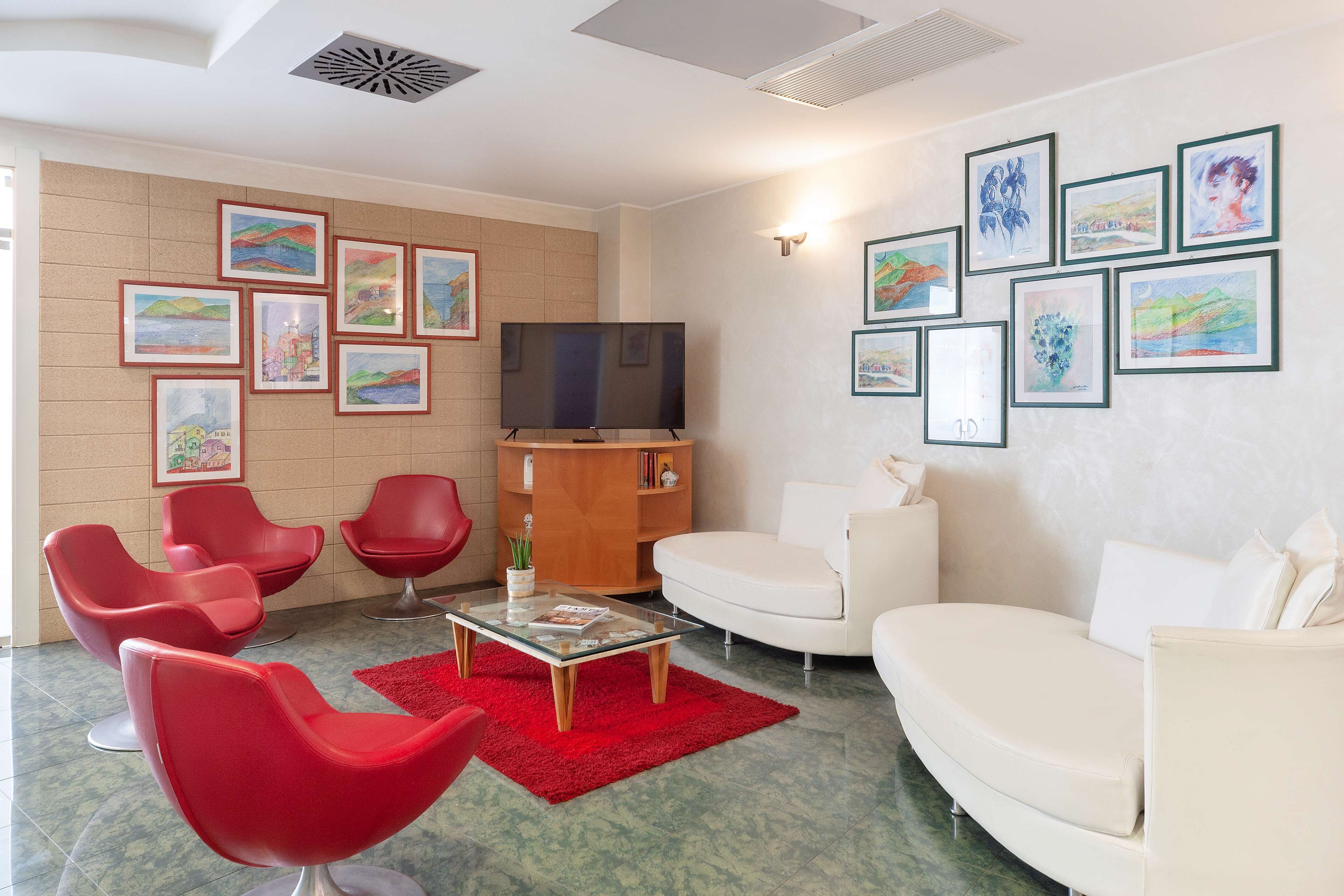 A modern living room with red and white furniture, a flat-screen TV, and various framed artworks on the walls.