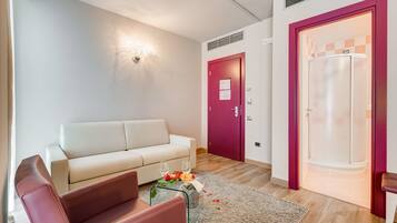 A modern living room with a white sofa, a glass coffee table with flowers, a red chair, and a red door leading to a bathroom with a white shower.
