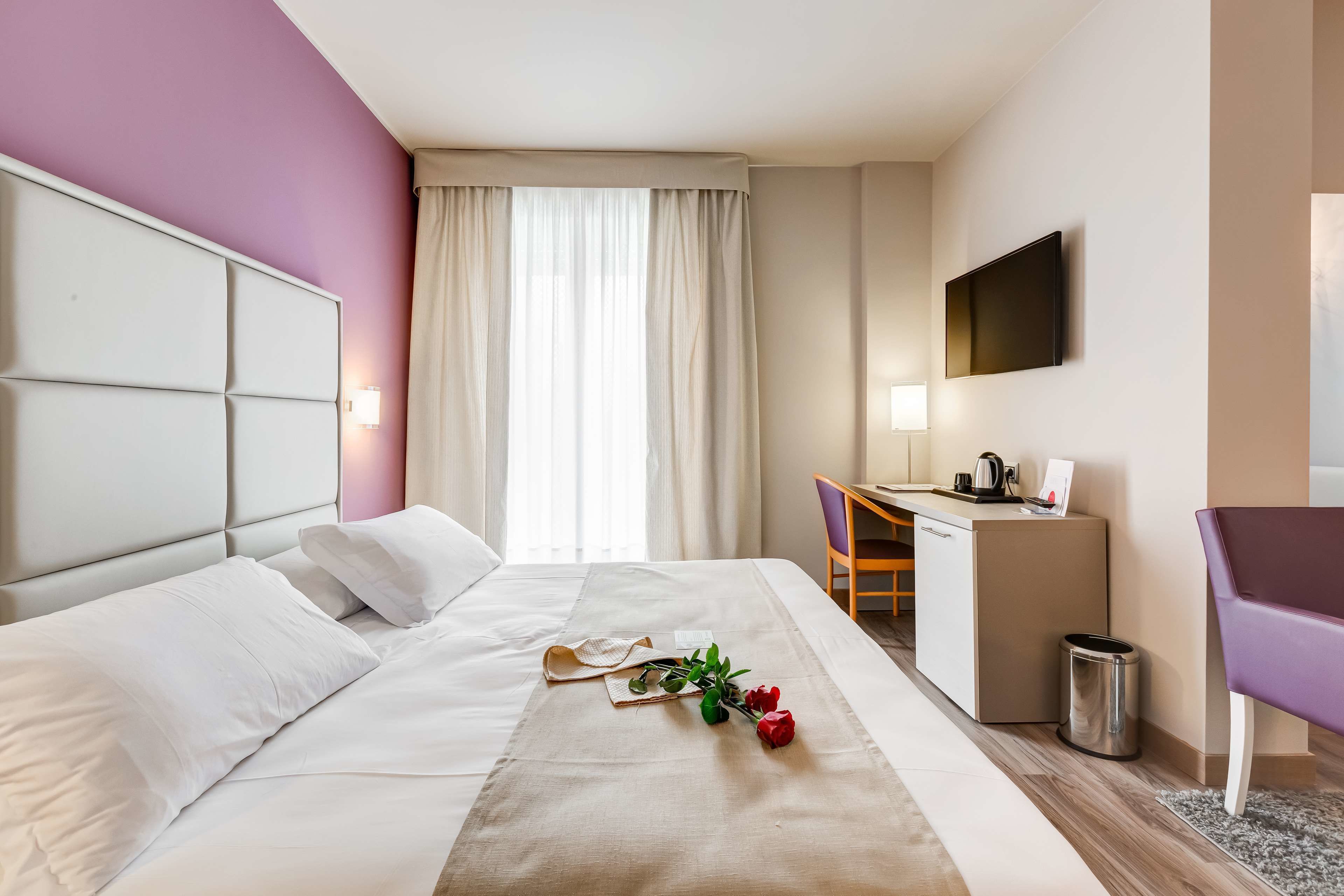 Une chambre d’hôtel avec un lit, un bureau, une chaise, une télévision et une fenêtre avec des rideaux.