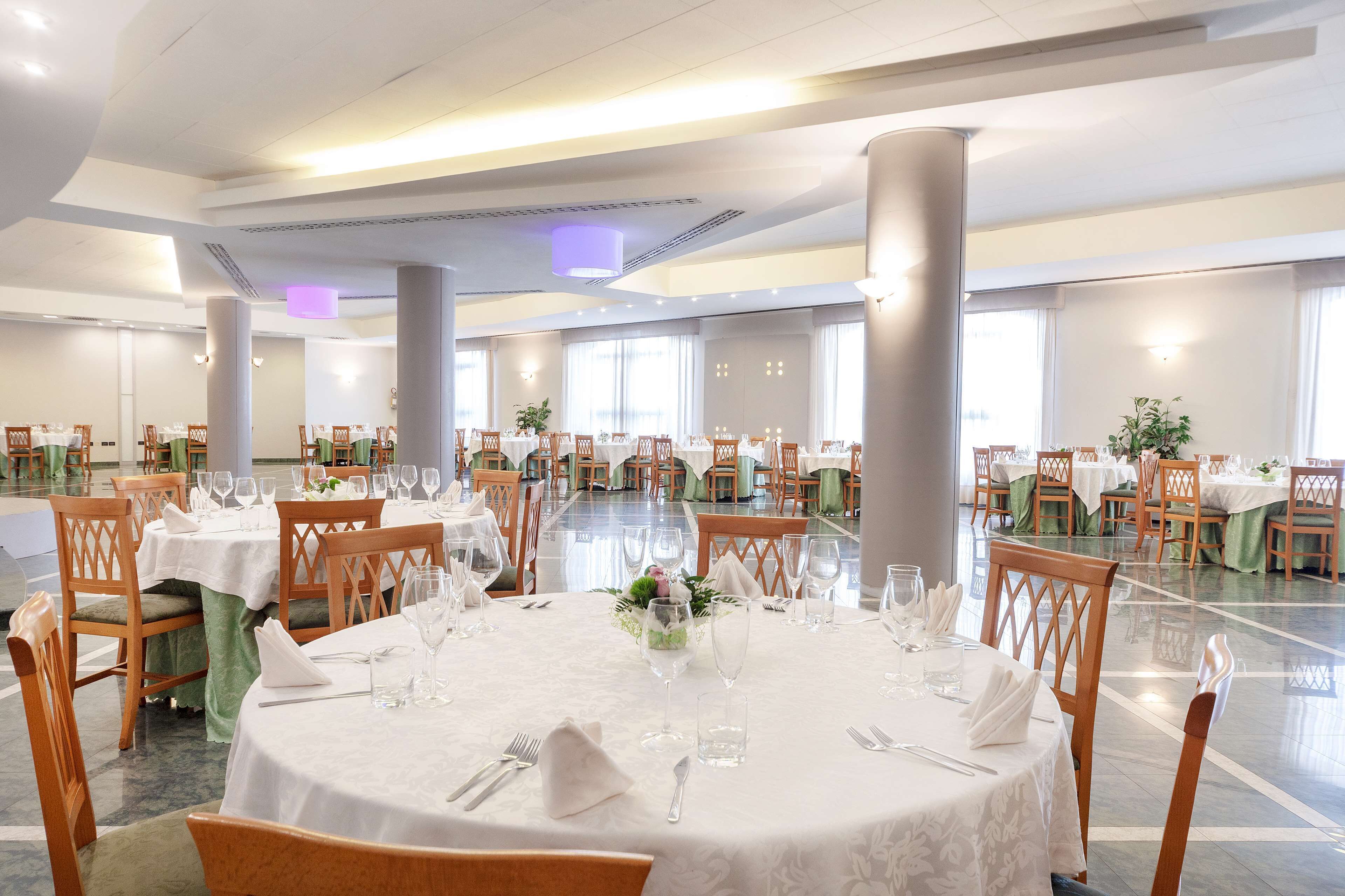 Un amplio salón de banquetes con mesas redondas dispuestas para comer, sillas de madera y un suelo pulido.