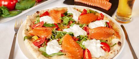 A plate of food with salmon, tomatoes, and greens, a glass of beer, and a fork and knife on a table.