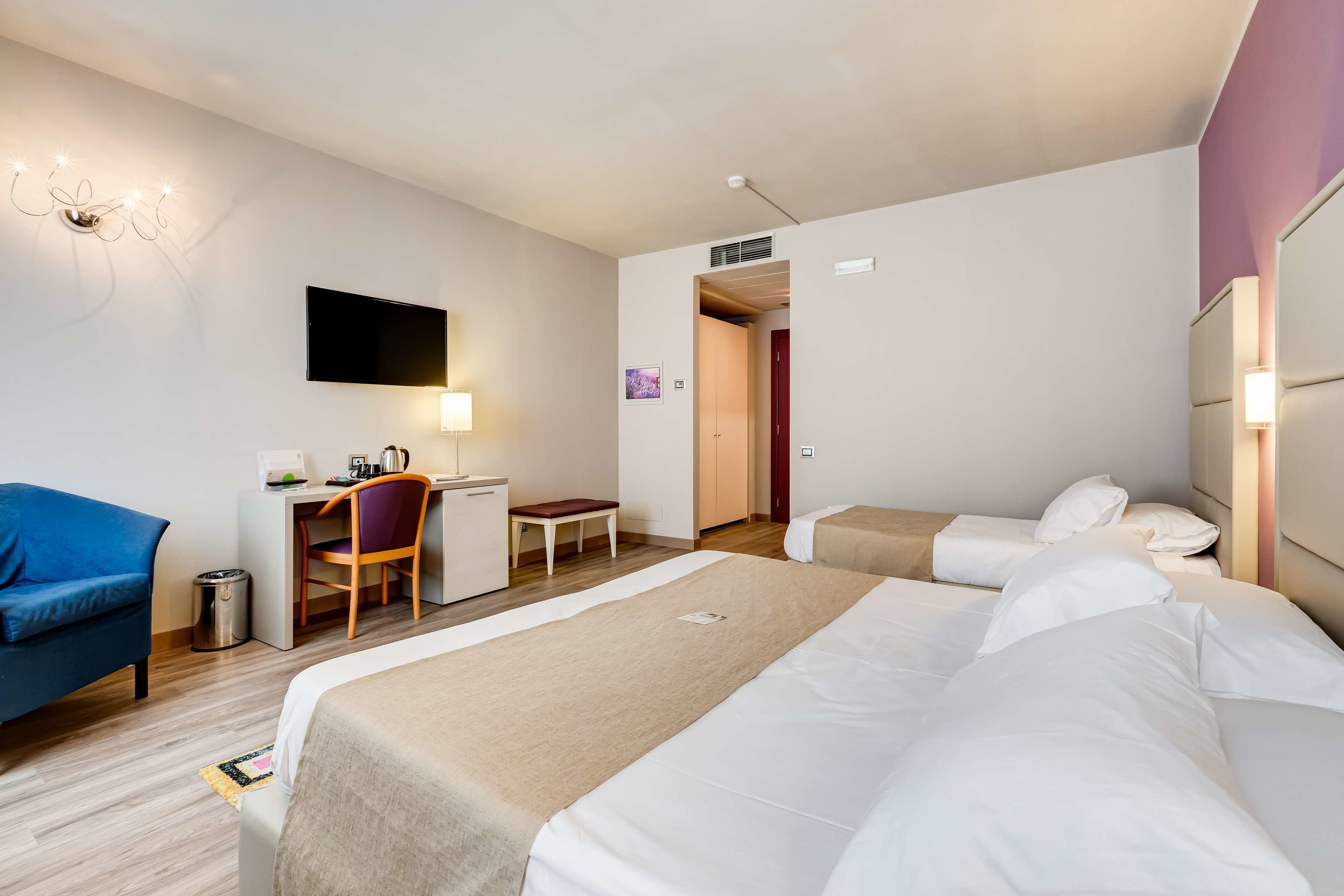Una habitación de hotel con dos camas, un escritorio con silla, televisión y un pequeño rincón de descanso.