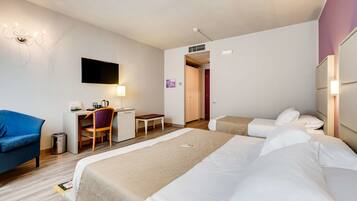 Una habitación de hotel con dos camas, un escritorio con silla, televisión y un pequeño rincón de descanso.