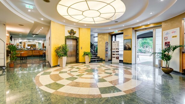 Un hall d’hôtel avec un sol à motifs à carreaux, un luminaire central et un comptoir de réception.