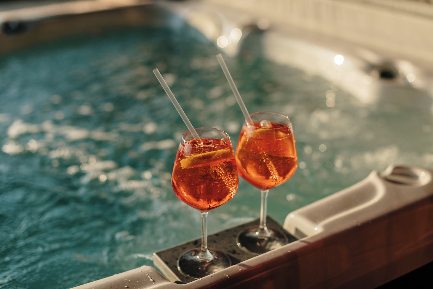 Two glasses of a red beverage with straws on a poolside table.