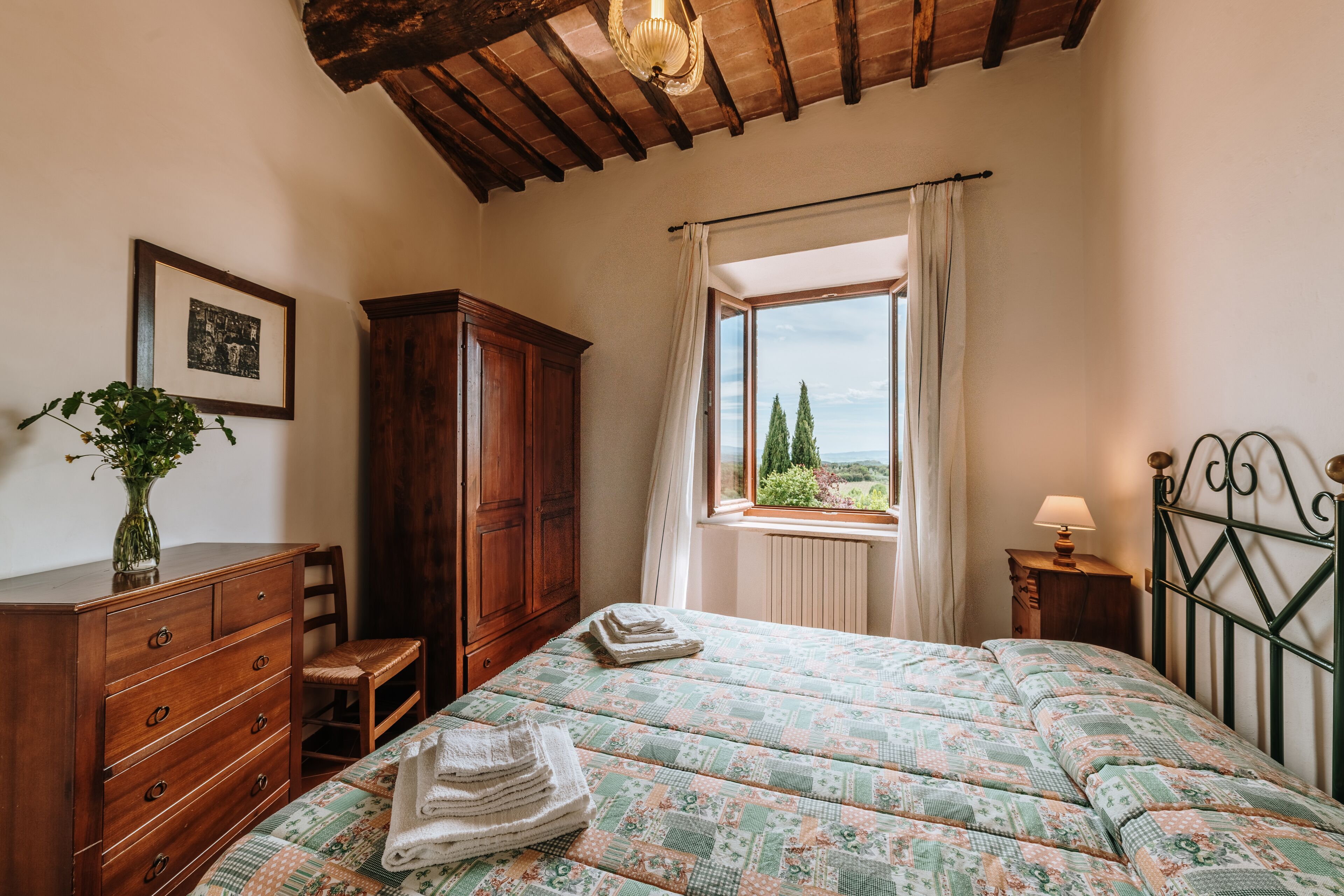 A bedroom with a bed, wooden dresser, and a window with a view of trees.