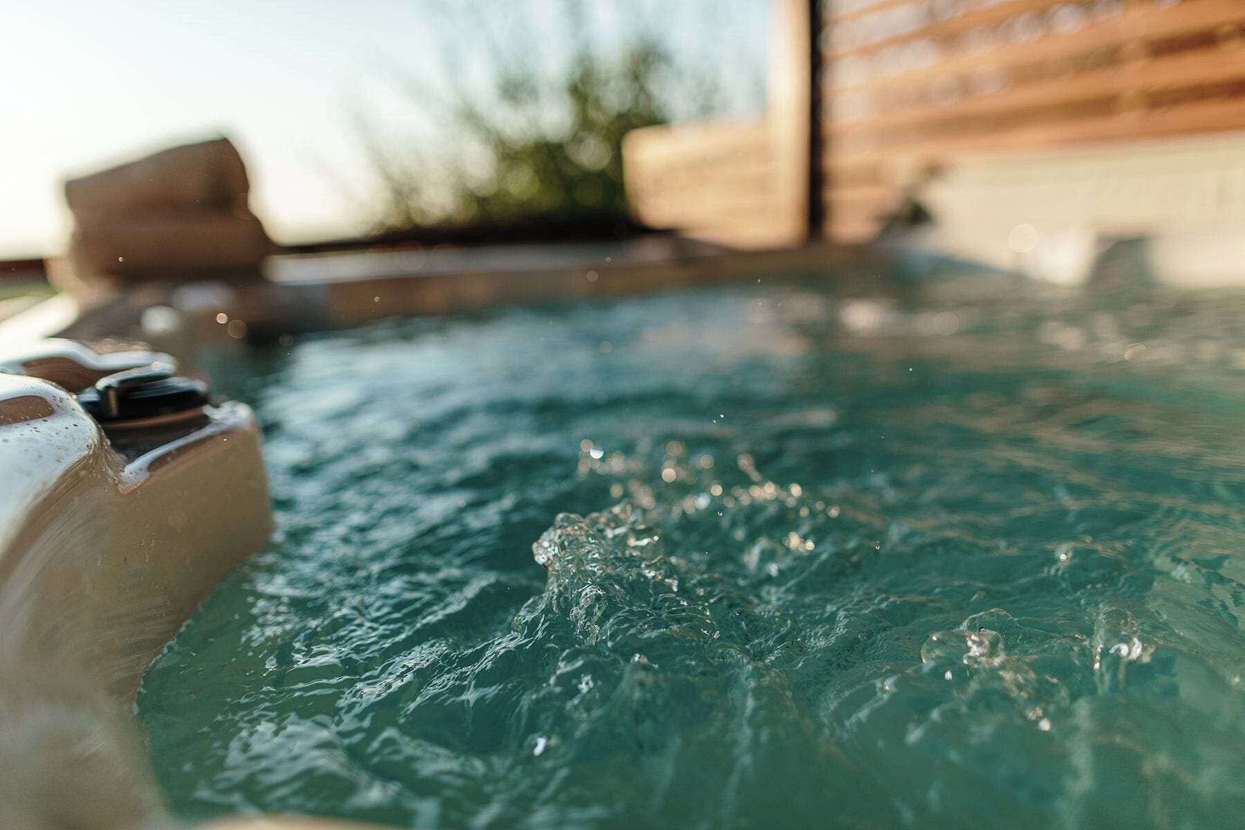 Een bubbelbad met opspattend water, een houten terras en een gebouw op de achtergrond.