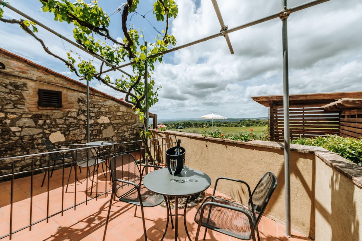Eine Terrasse mit Tisch und Stühlen, eine Steinmauer und Blick ins Grüne.