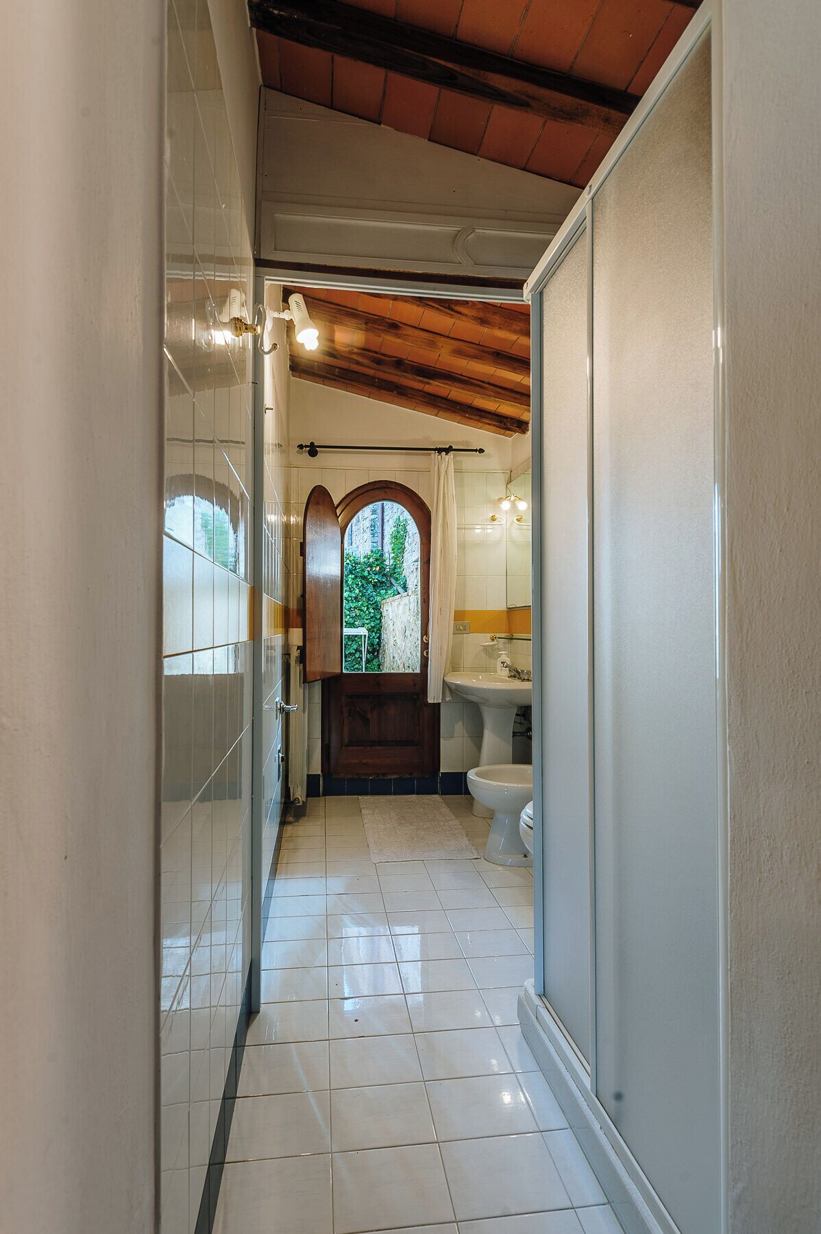 Une salle de bain avec un sol carrelé, une fenêtre donnant sur un espace verdoyant, un lavabo et des toilettes.