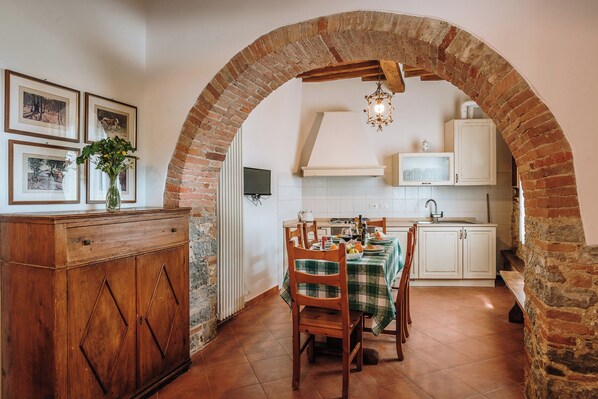 A rustic dining area with a brick archway, wooden furniture, and a tiled floor.