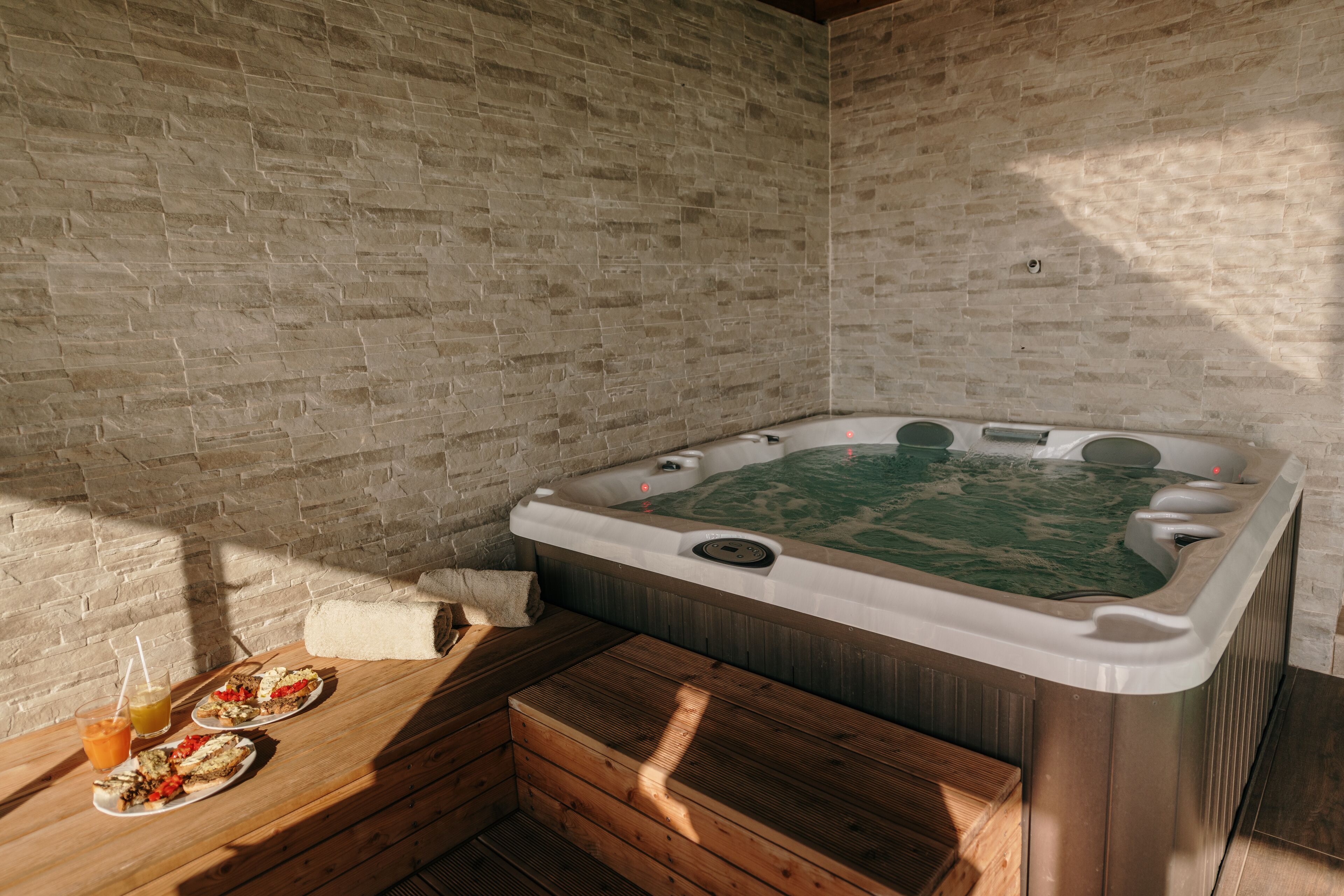 A spa room with a hot tub, wooden benches, and a brick wall.