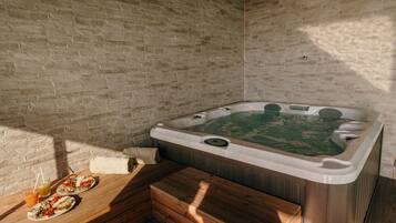 A spa room with a hot tub, wooden benches, and a brick wall.
