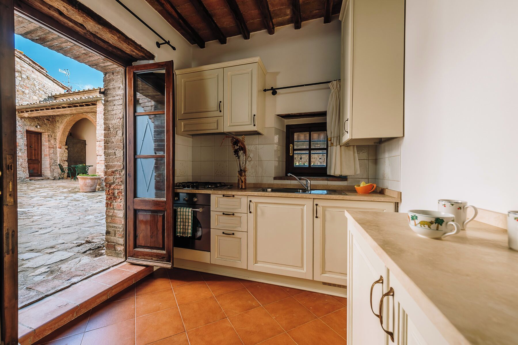 Una cocina con armarios blancos, salpicadero de azulejos y ventana con vista a un patio.