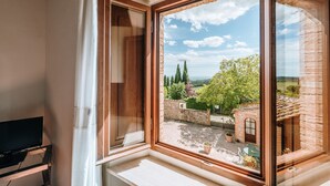 A room with a large window overlooking a courtyard with a brick building, trees, and a clear sky. - Villa di Sotto (Castelnuovo Berardenga)