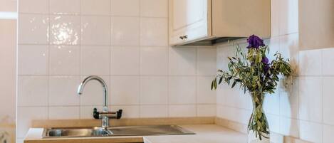 Una cocina con azulejos blancos, un lavamanos de acero inoxidable y un florero con flores en la encimera.