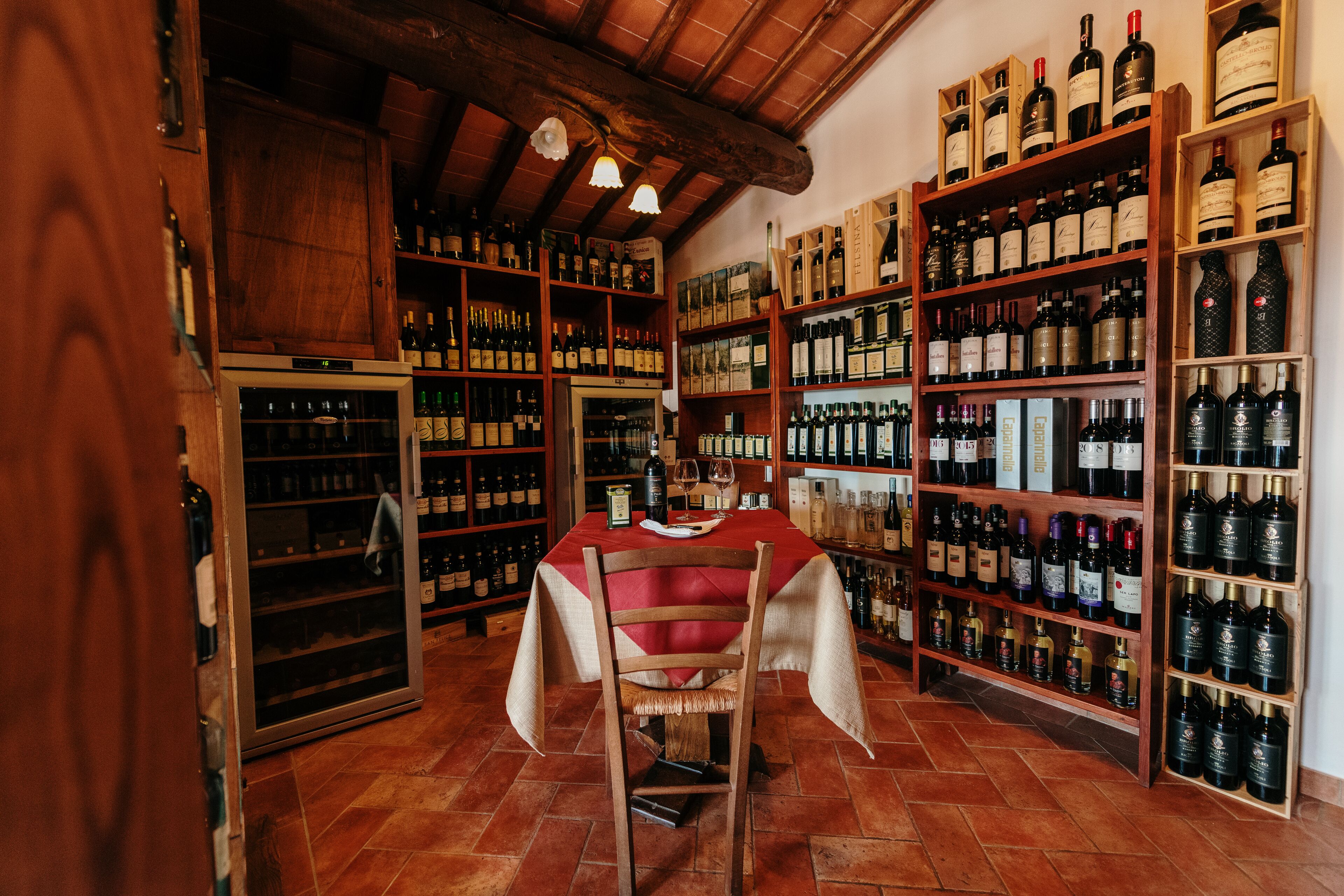 A wine cellar with wooden shelves stocked with wine bottles, a table with a red tablecloth, and a wine cooler.