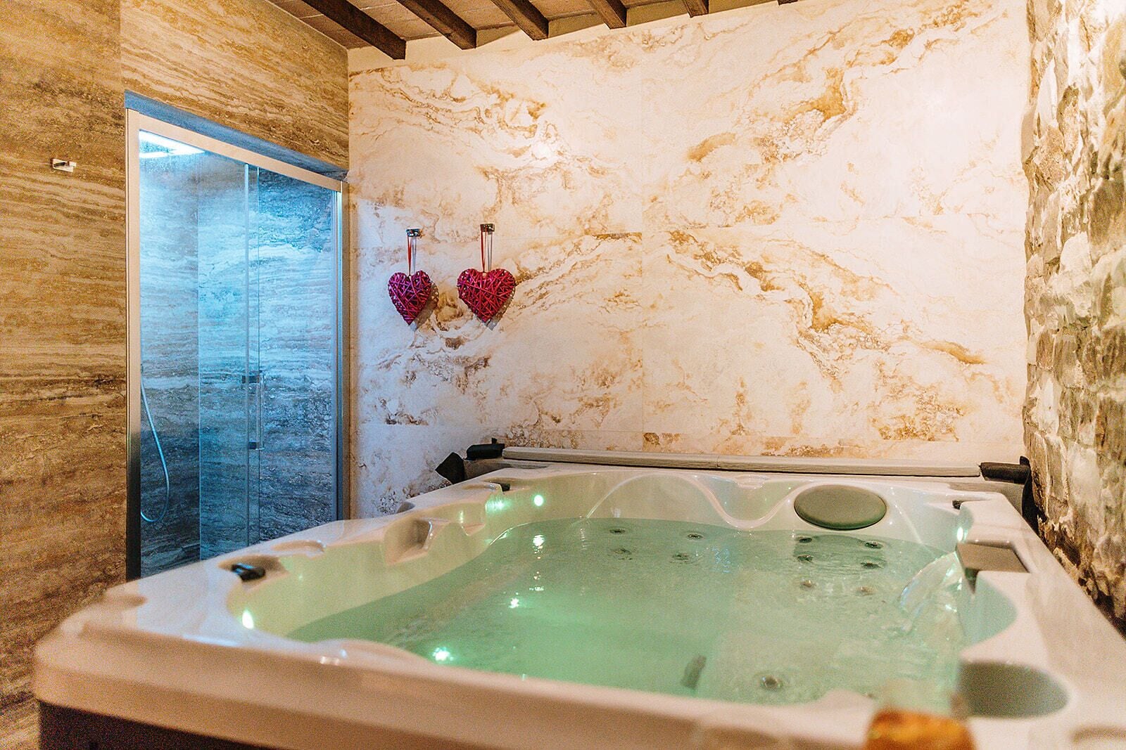 A spa room with a marble wall, a glass-enclosed shower, and a hot tub.