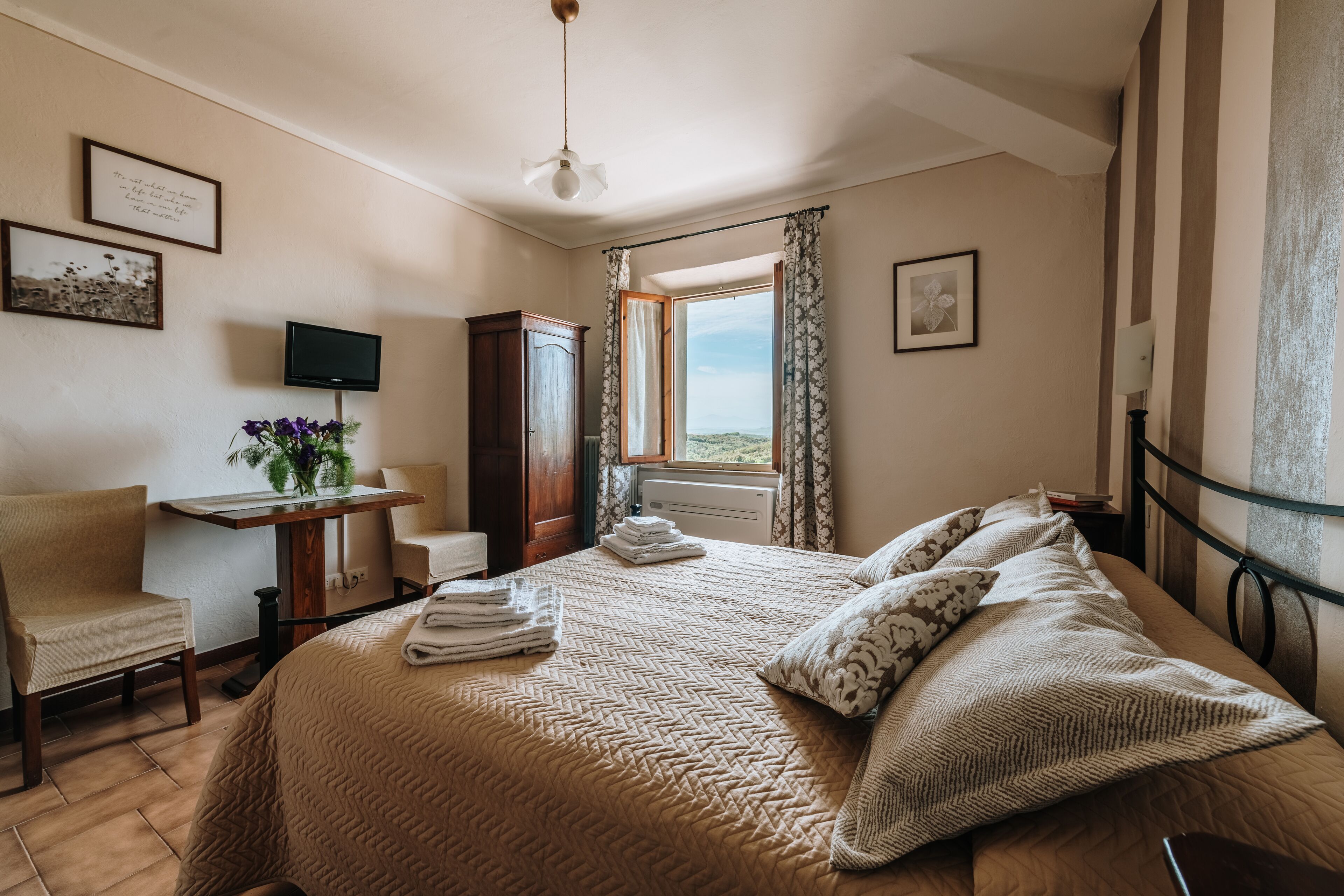 Una habitación de hotel con cama, escritorio, silla, televisor y ventana con cortinas.