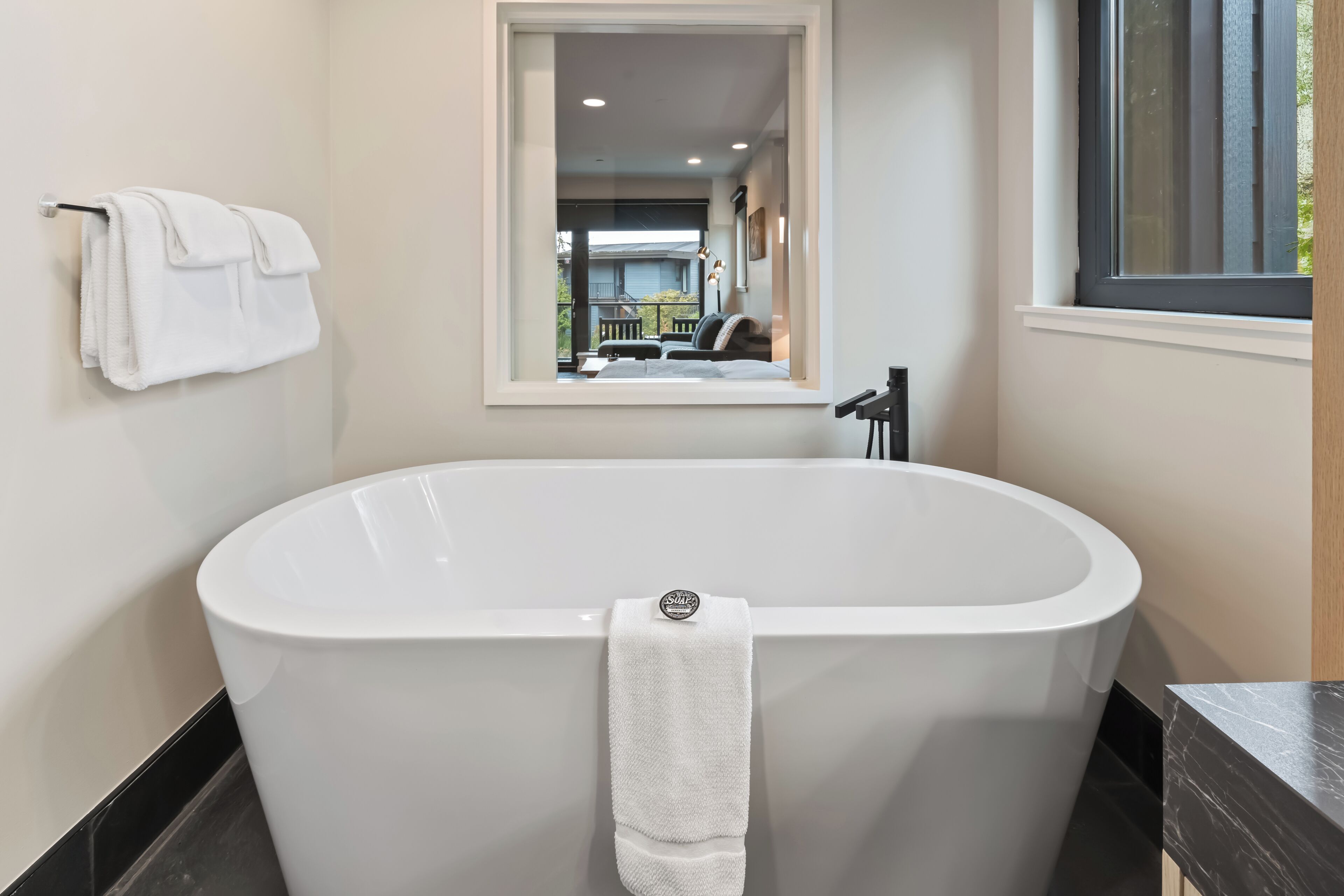 A modern bathroom with a freestanding bathtub, a towel rack, and a window with a view of the outside.