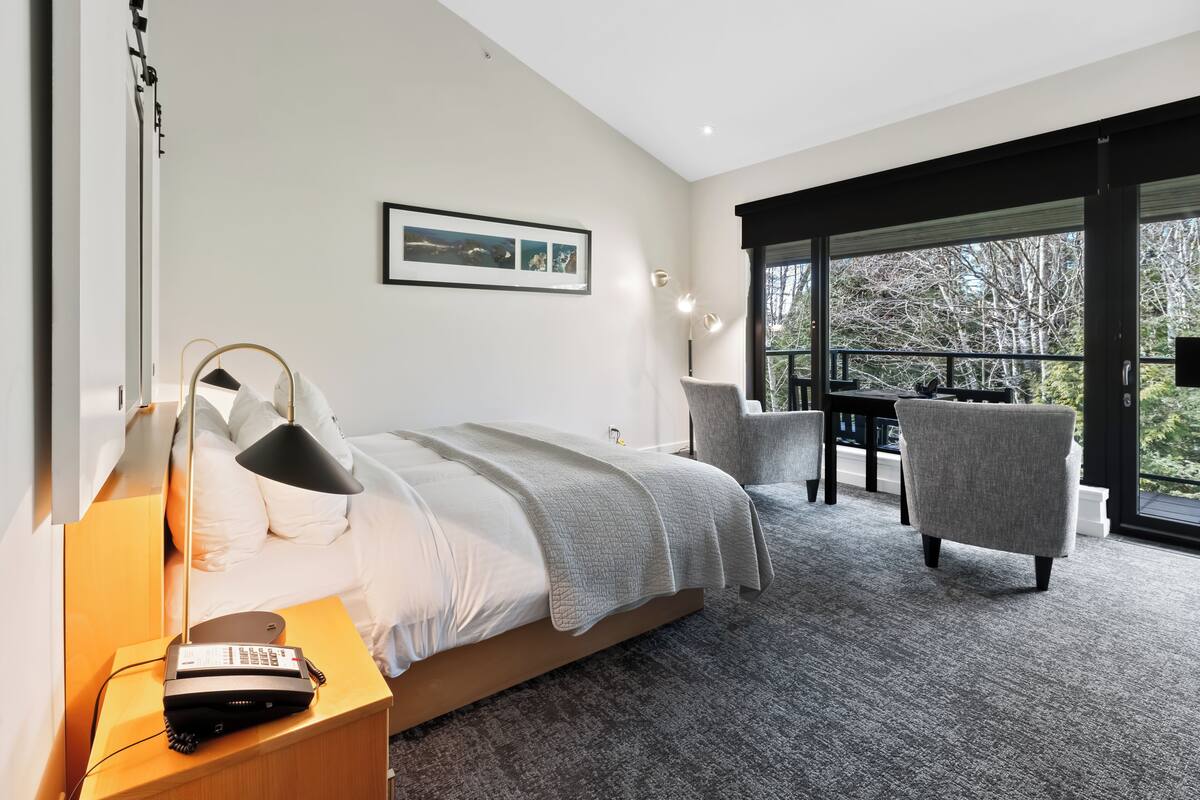Een moderne hotelkamer met een groot bed, een bureau en een stoel. Er is een raam met uitzicht op bomen.
