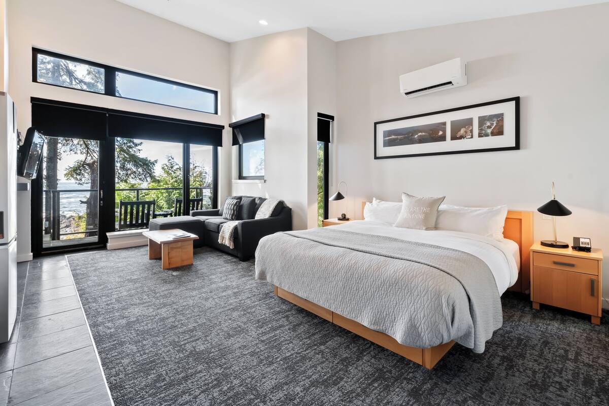 Een moderne slaapkamer met een groot bed, een bank, een klein tafeltje en een nachtkastje. Er is een raam met uitzicht op het omliggende landschap.