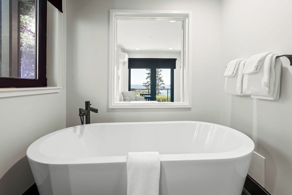 A modern bathroom with a freestanding bathtub, a window with a view of the outdoors, and a towel rack with towels.