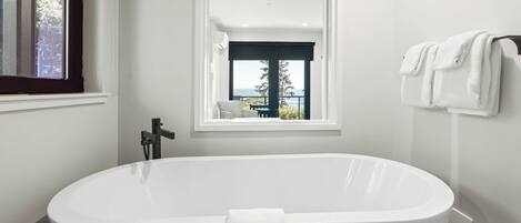 A modern bathroom with a freestanding bathtub, a window with a view of the outdoors, and a towel rack with towels.
