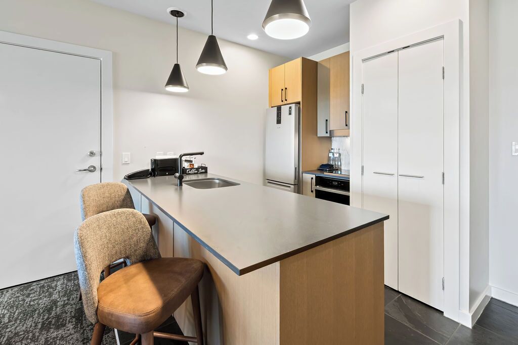 Une cuisine moderne dotée d’un îlot central, de tabourets de bar, de luminaires suspendus et d’un réfrigérateur.