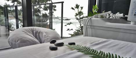 Une salle de spa équipée d’un lit, d’une balustrade en verre et offrant une vue sur l’océan.