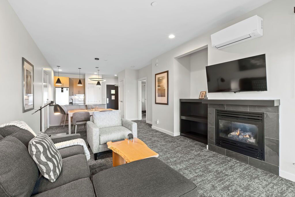 A modern living room with a fireplace, a television mounted above it, and a dining area in the background.