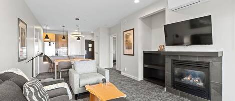 A modern living room with a fireplace, a television mounted above it, and a dining area in the background.