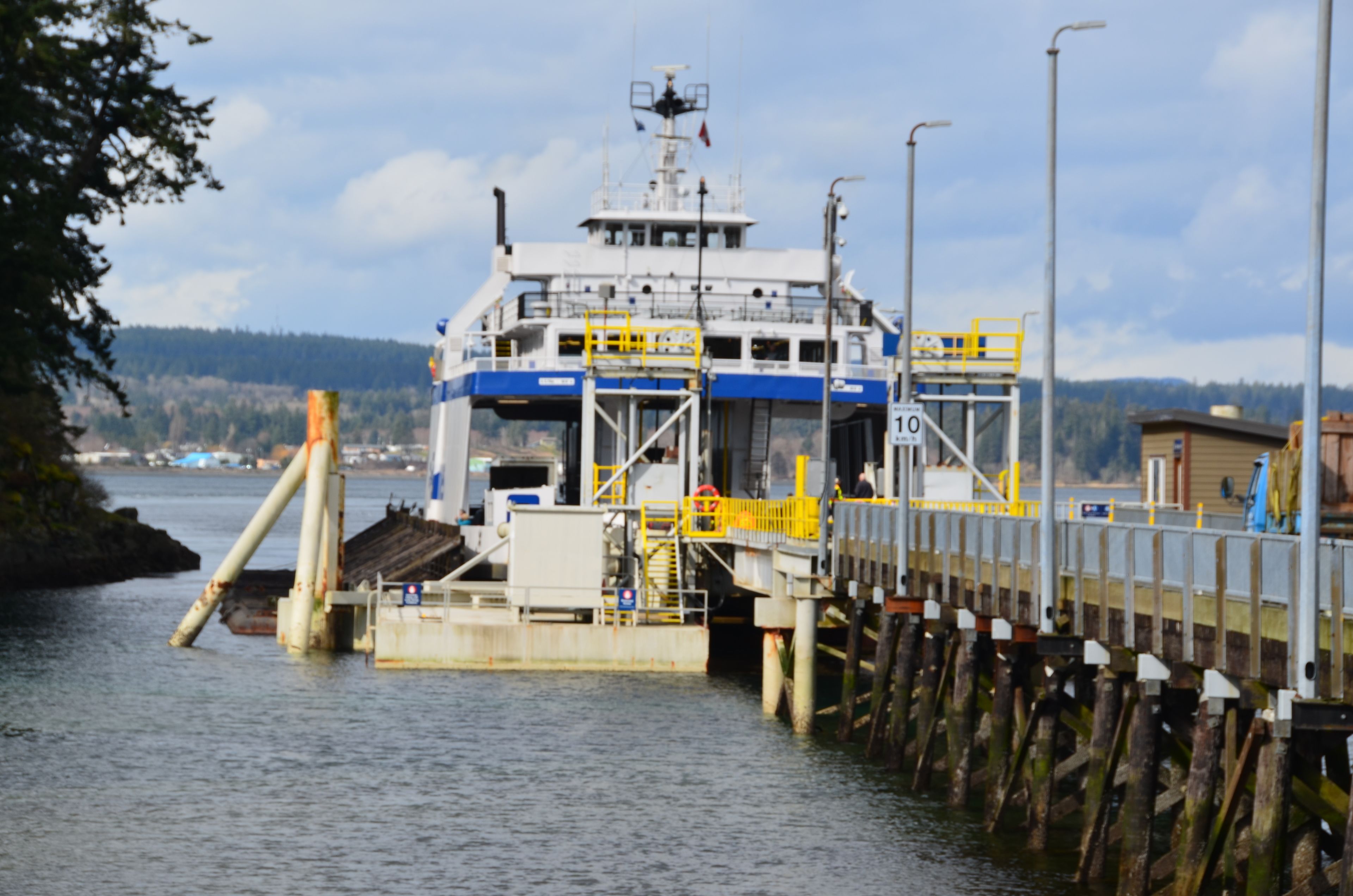 Um ferry atracado em cais, com vista para a água e paisagem arborizada ao fundo.